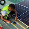 Technician working on solar panel installation with cables and tools on a sunny day.