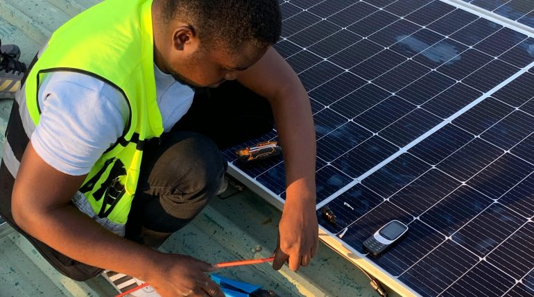 Technician working on solar panel installation with cables and tools on a sunny day.